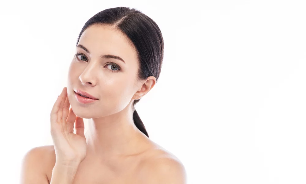 A woman with flawless, glowing skin gently touching her face, showcasing the radiant results of Skinvive treatment in Portsmouth, NH.